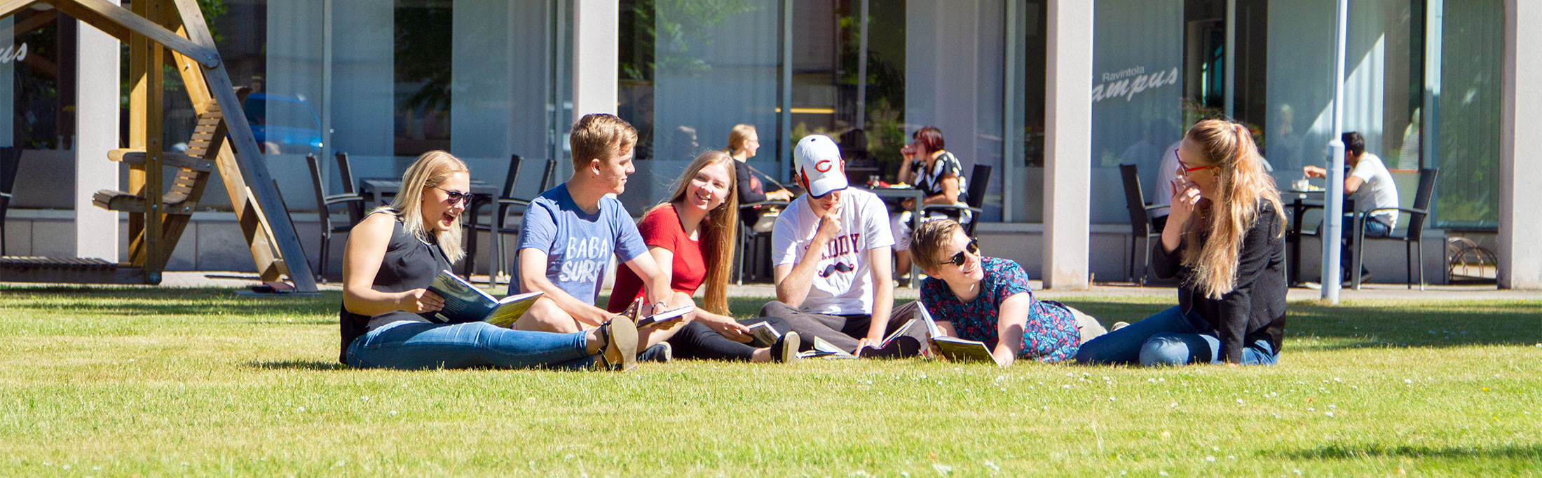 Opiskelijoita istumassa nurmikolla Mikkelin kesäyliopiston rakennuksen edessä.